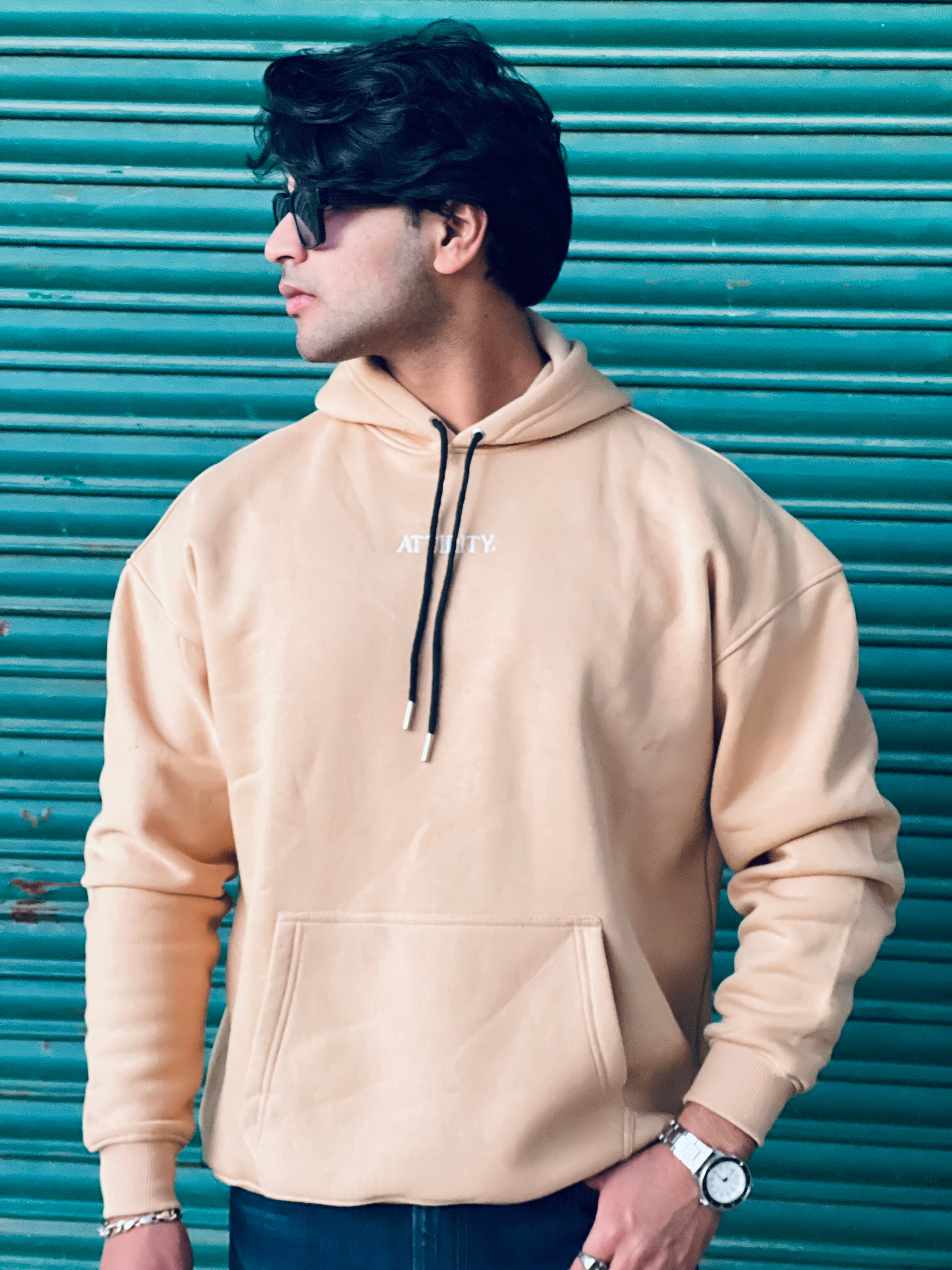 Man wearing a beige hoodie with a brand logo against a teal shutter background