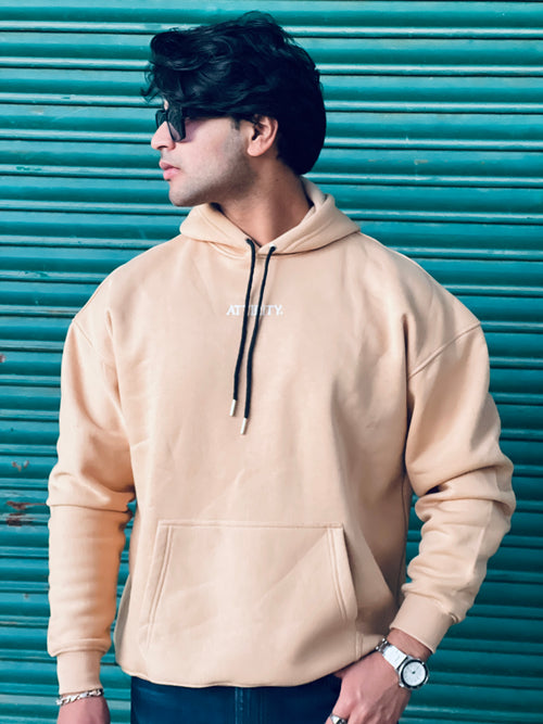 Man wearing a beige hoodie with a brand logo against a teal shutter background