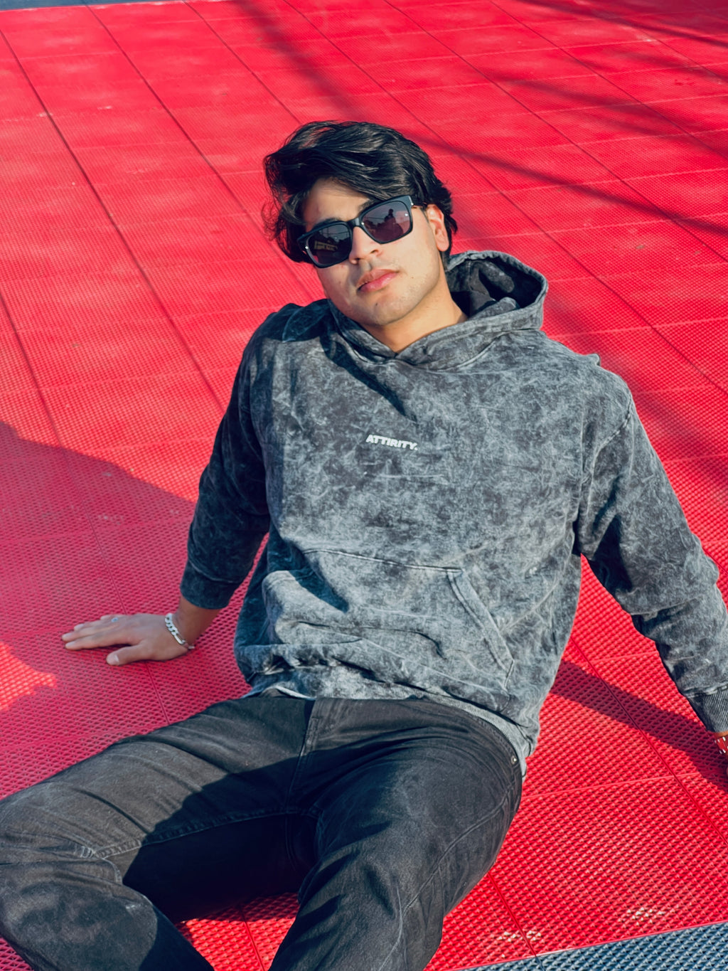 Person wearing a gray hoodie (acid wash) from Attirity, sitting on a red surface