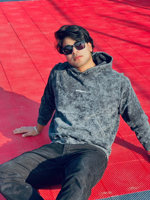 Person wearing a gray hoodie (acid wash) from Attirity, sitting on a red surface