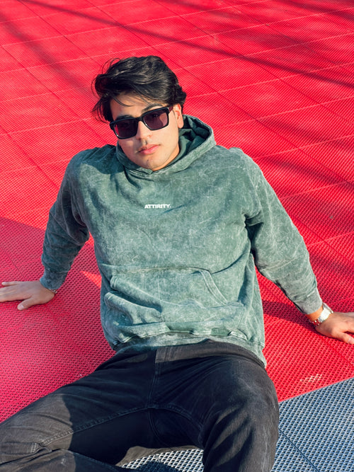 Person wearing a green hoodie (acid wash hoodie) with a brand logo, sitting on a red and blue checkered surface.