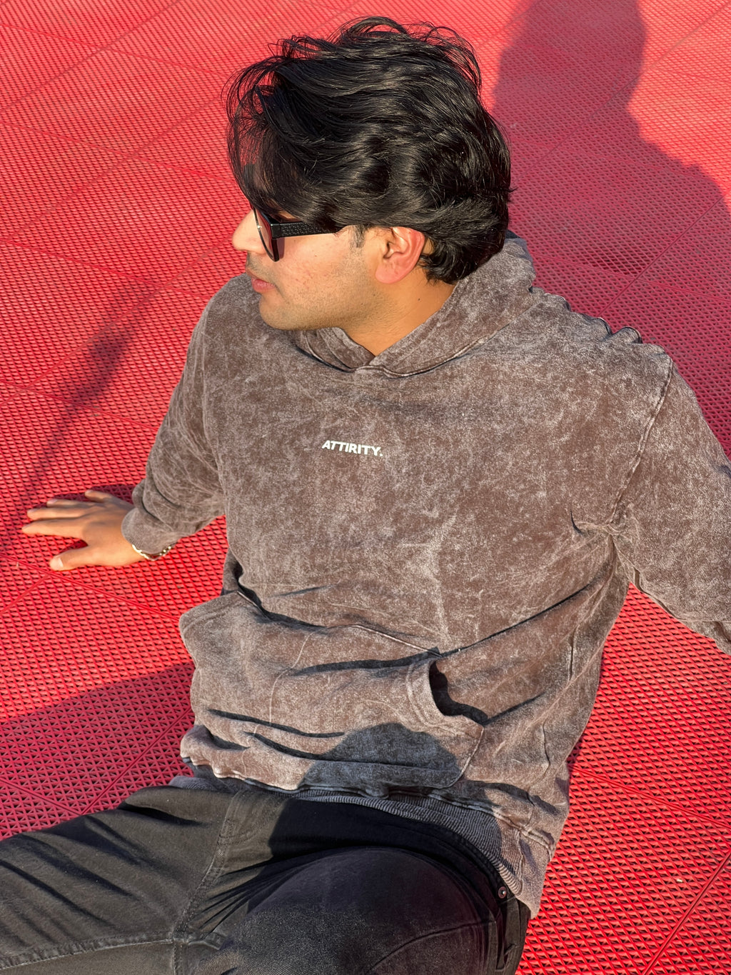 Person sitting on a red mat wearing a brown acid wash hoodie with 'ATTIRITY' branding.